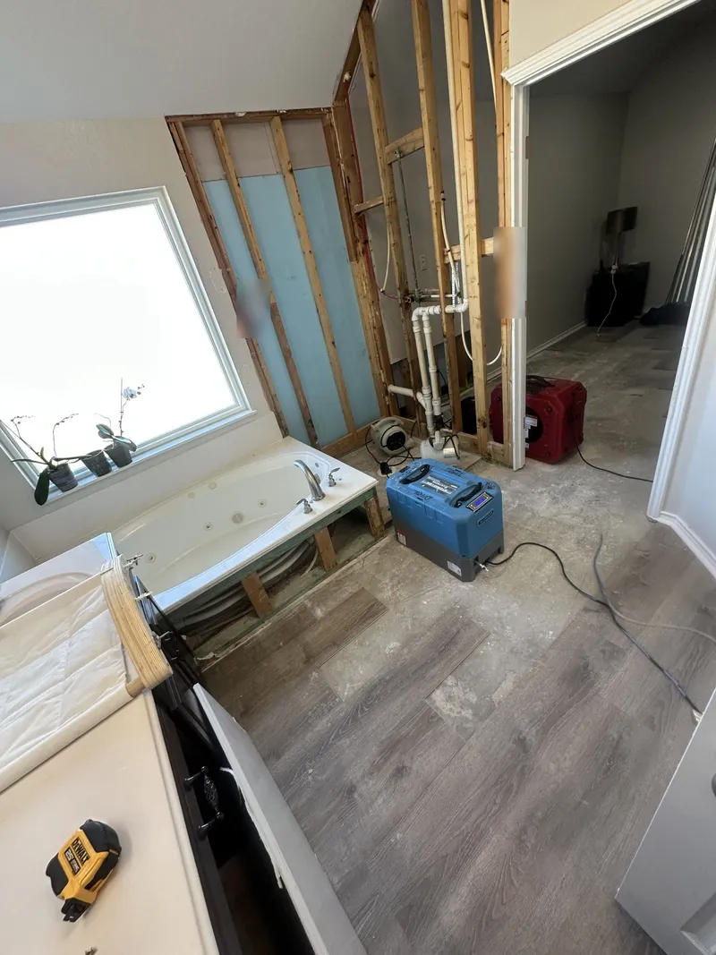 Primary bathroom with the wet drywall removed to the studs behind a jetted tub, plumbing exposed and a dehumidifier on the floor