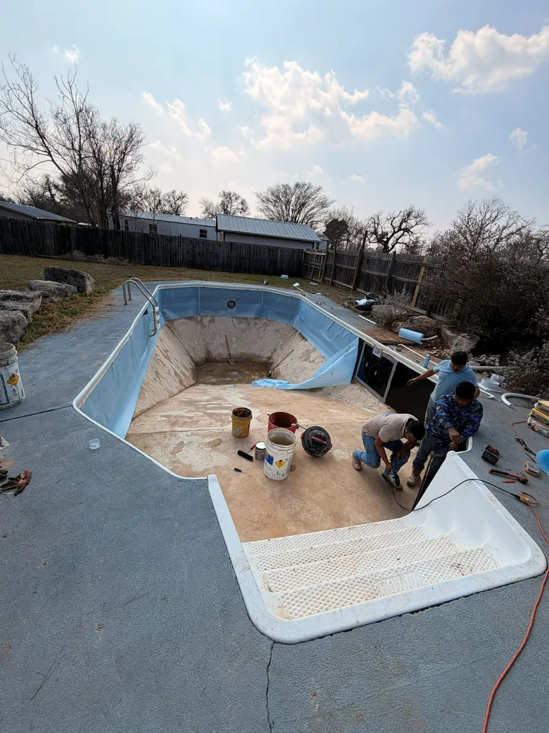 Empty vinyl liner pool with the old liner pulled back from the walls and crew members working by the entry steps